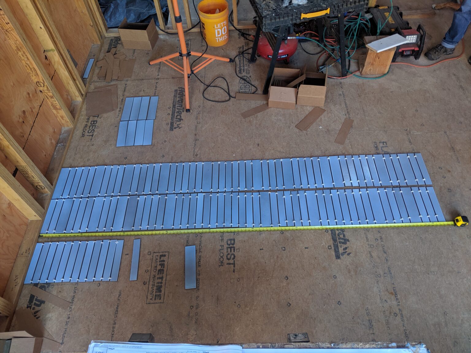 Story pole made from the real blue tile: courses laid out with spacers on the subfloor and a tape measure pulled alongside, with the walls still open framing